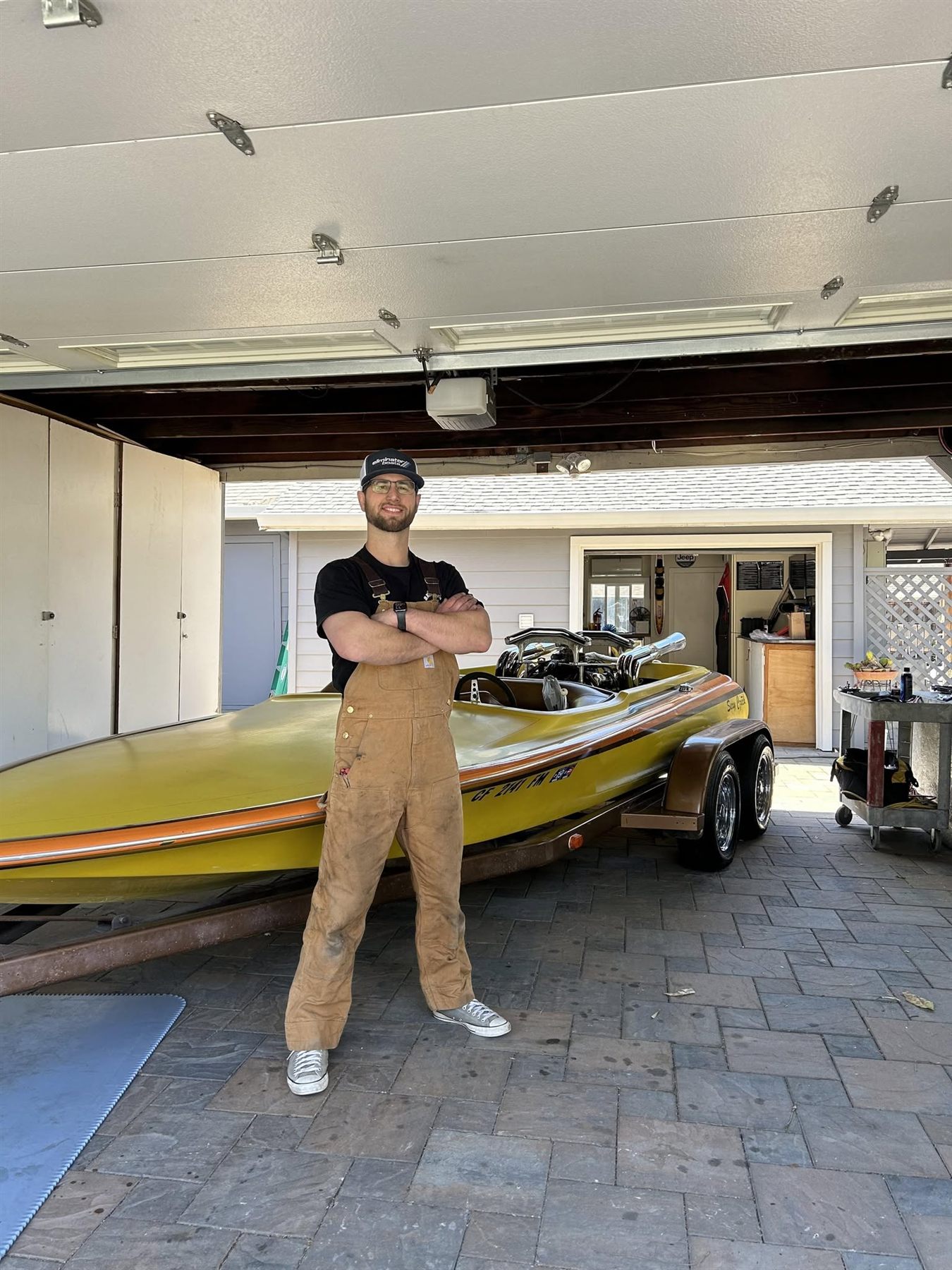 The owner of Full Throttle Marine standing with arms crossed in front of a gold and orange classic jet boat at the Concord shop.