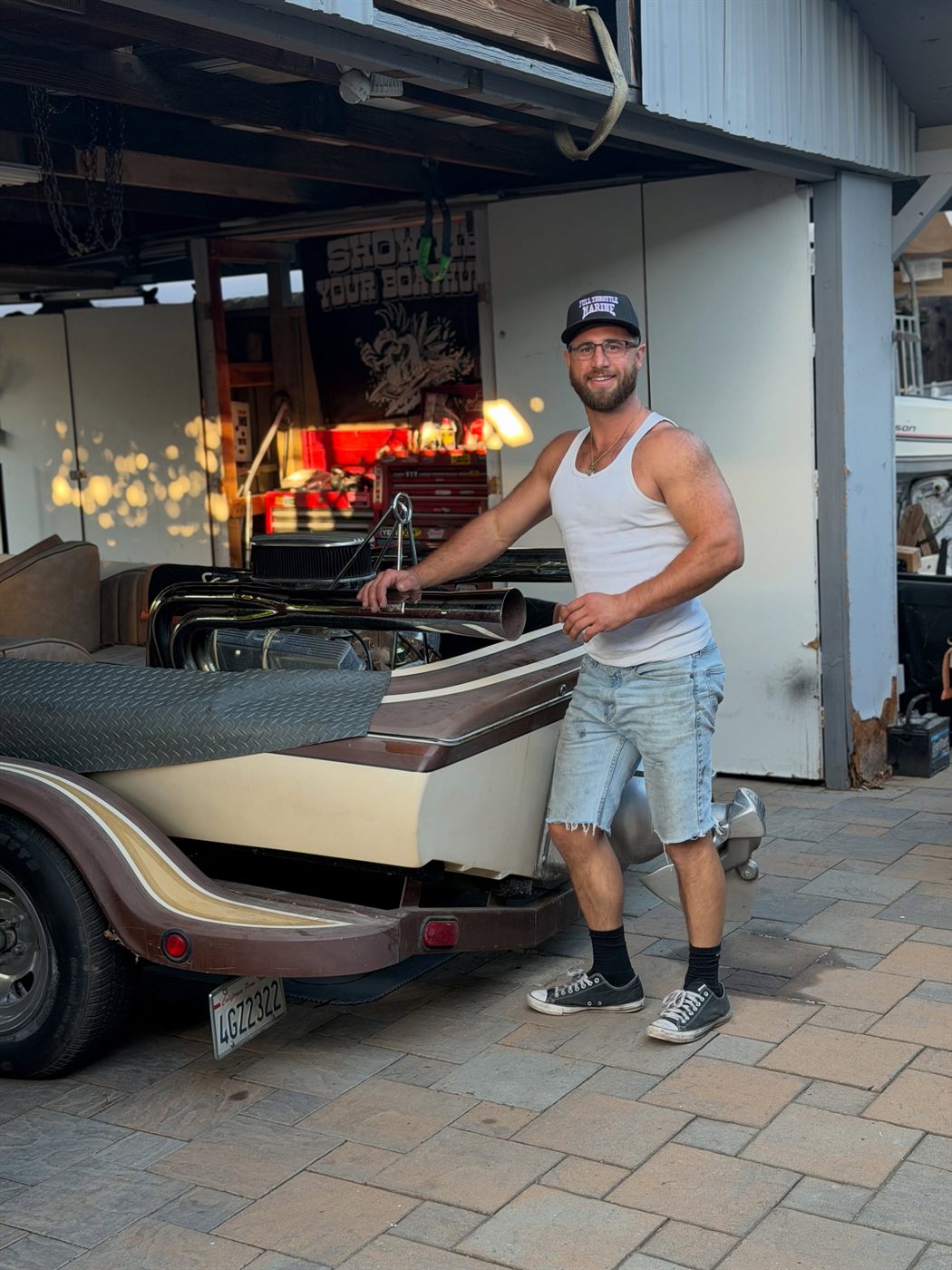 Classic jet boat on a trailer outside the shop at dusk, engine cover off.