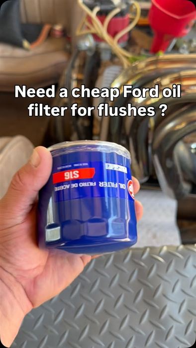 A low-cost spin-on oil filter held up in the engine bay, used for flush cycles.